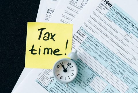 Tax return form with an alarm clock sitting on top and a post-it note reading 'Tax time!'